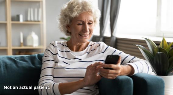 Woman smiling at her phone while sitting on a couch.