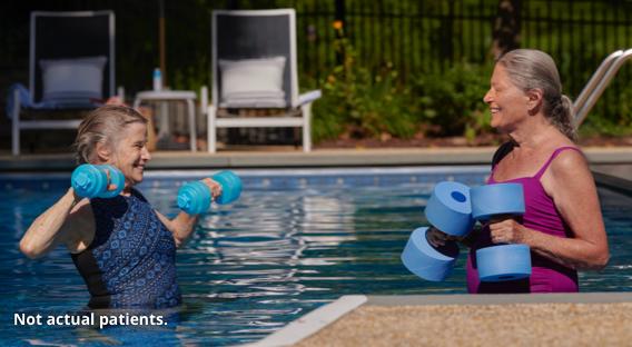 Two women exercising in a pool with weights.