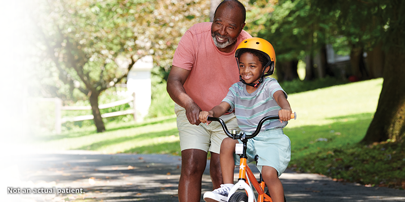 Older man pushing a boy on a bike.